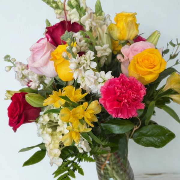 Mixed bouquet of roses, carnations, and white filler flowers in a glass vase