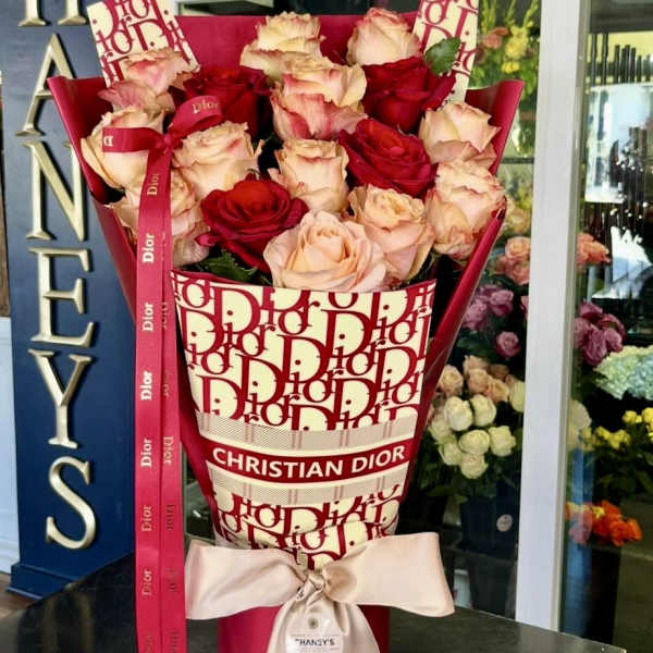Bouquet of red and blush roses in a Dior-patterned wrap with a ribbon