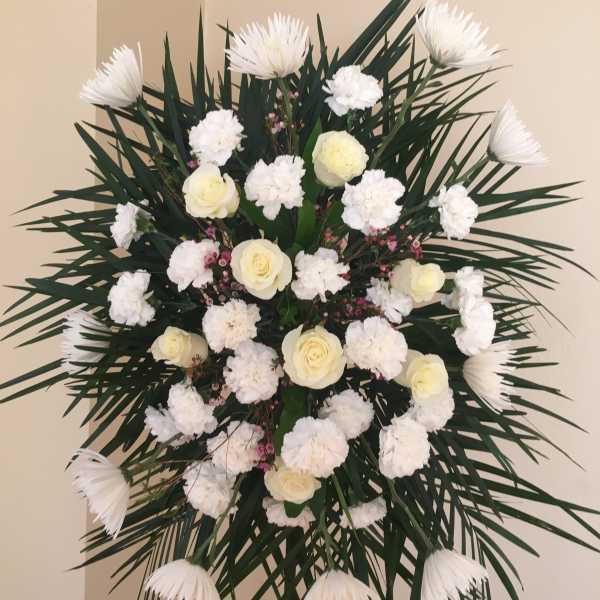 White floral standing spray with roses and carnations on dark palm fronds