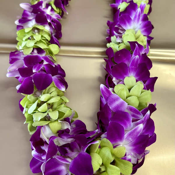 Purple and green orchid lei on a beige surface