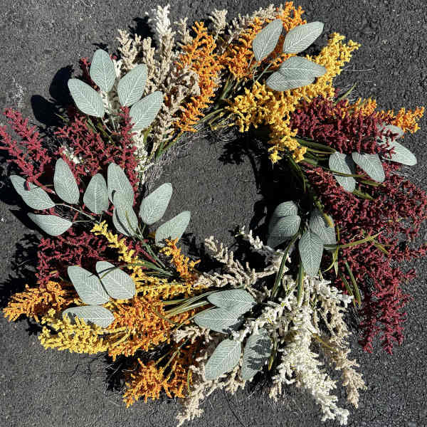 Circular wreath of colorful dried flowers on dark pavement