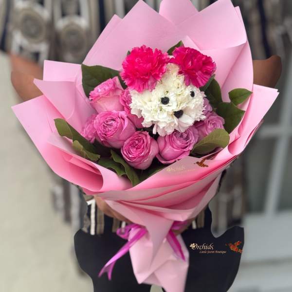 Pink bouquet with roses, carnations, and white flowers wrapped in pink paper