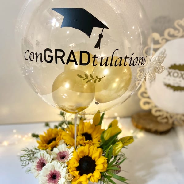 Graduation balloon above a sunflower and daisy arrangement