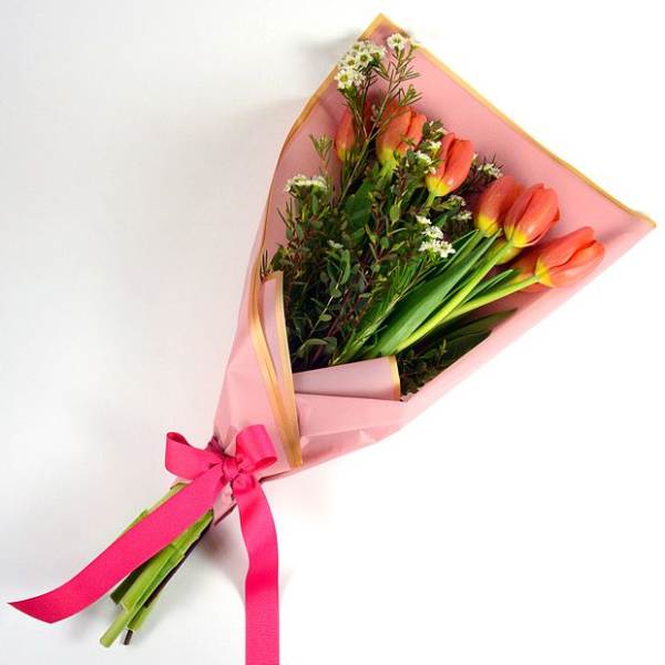 Pink-wrapped bouquet of orange tulips tied with a bright ribbon