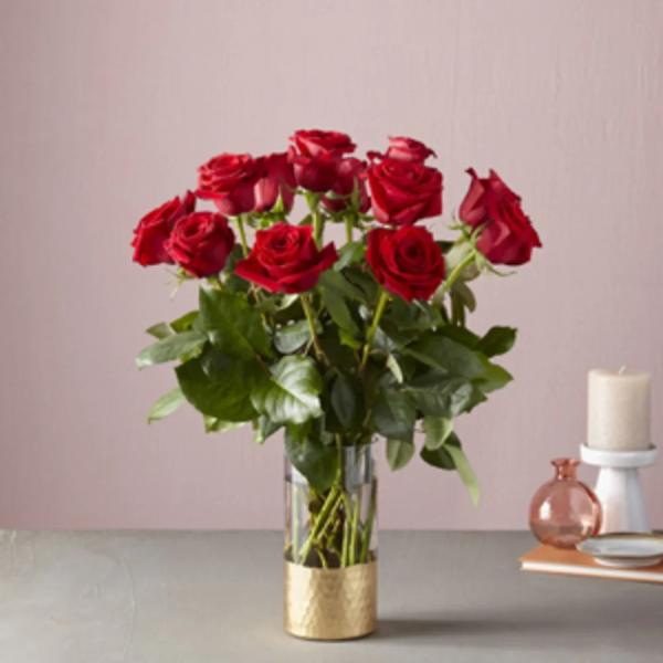Red roses arranged in a clear glass vase with a gold base