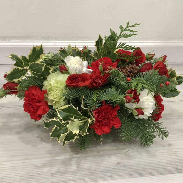 Low floral arrangement with red and white blooms and evergreen accents