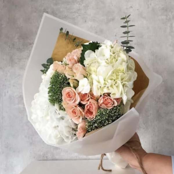 Handheld bouquet of white hydrangeas and peach roses wrapped in white paper