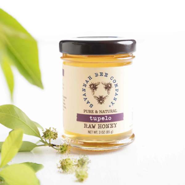 Jar of tupelo raw honey with green leaves beside it
