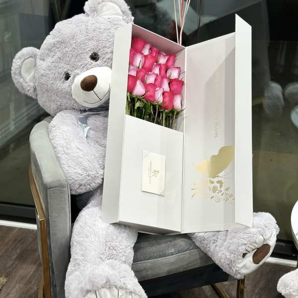 Pink roses in a white gift box beside a large gray teddy bear