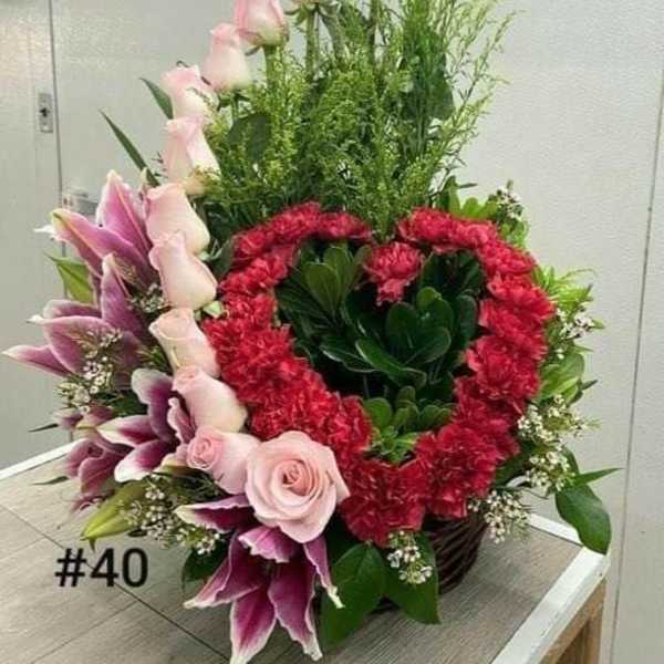 Tall floral arrangement with pink roses, lilies, and red carnations in a basket