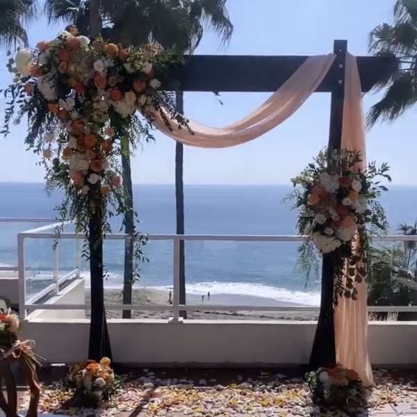 Floral wedding arch with peach draping overlooking the ocean