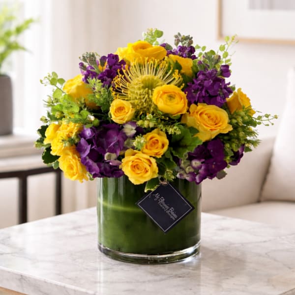 Yellow roses and purple flowers arranged in a glass vase