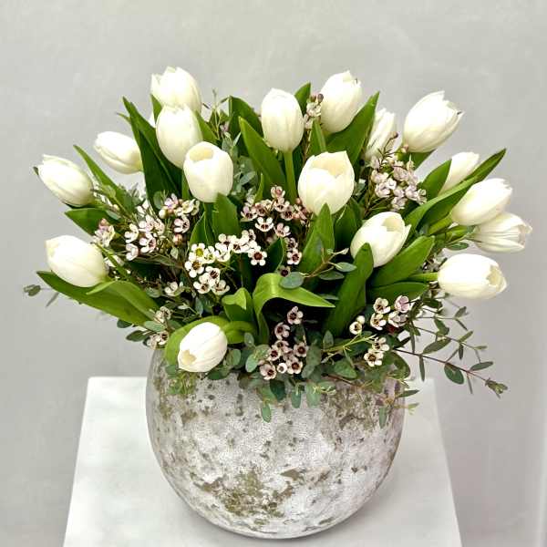 White tulips arranged in a round silver vase with small pink-white filler flowers.