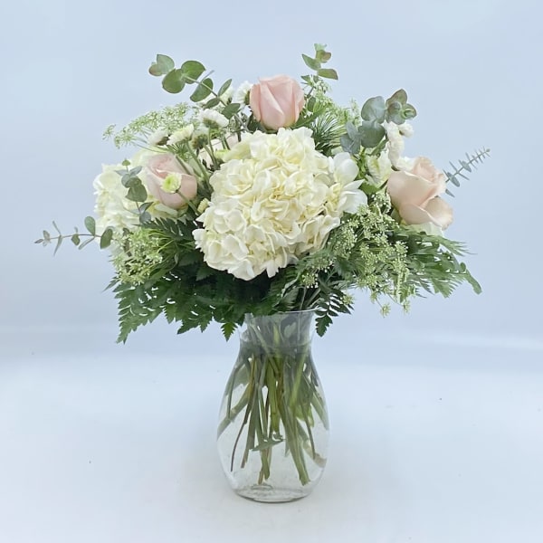 White hydrangea and pale pink roses in a clear glass vase