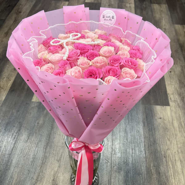 Pink and blush rose bouquet wrapped in pink paper with a ribbon, in a glass vase