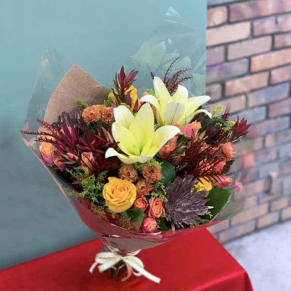 Bouquet of yellow lilies, roses, and mixed blooms wrapped in paper