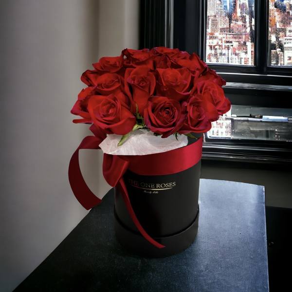 Red roses arranged in a black round box with a red ribbon