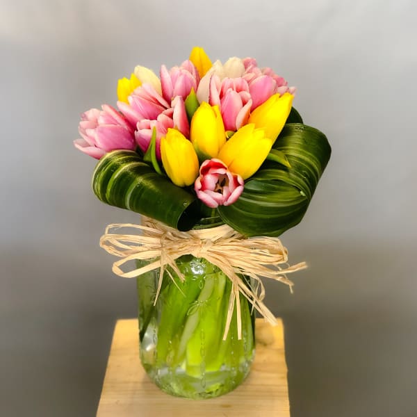 Pink and yellow tulips arranged in a glass vase with a raffia bow.
