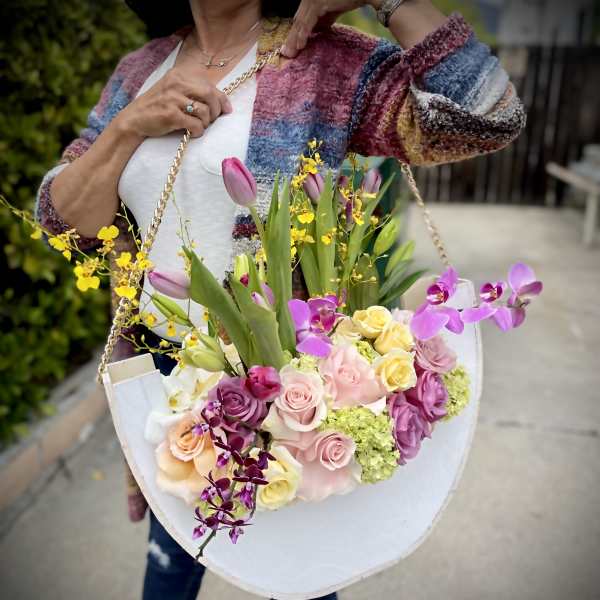 Woman holding a large pastel bouquet in a white tote-style container