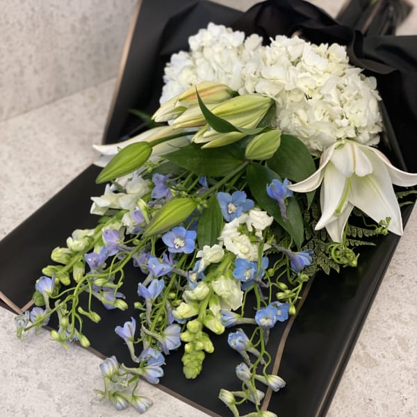 White hydrangeas and lilies with blue flowers in black wrapping
