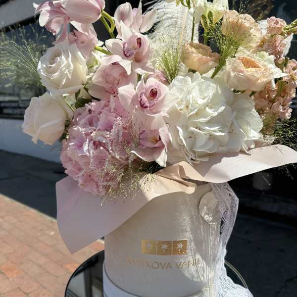 Pastel bouquet with pink orchids, white roses, and hydrangeas in a round hat box