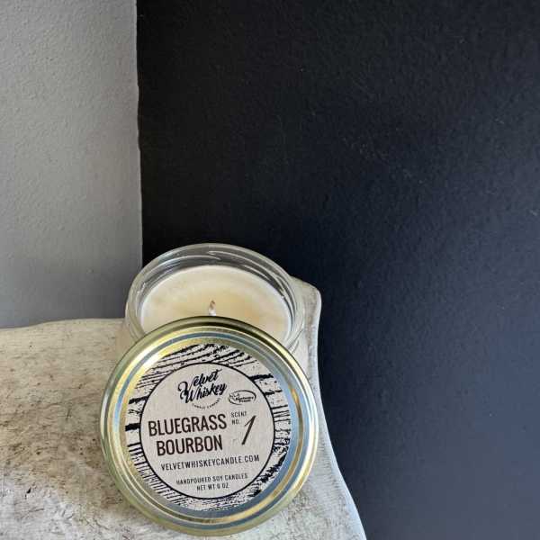 A jar candle with a labeled lid sits on a stone surface.