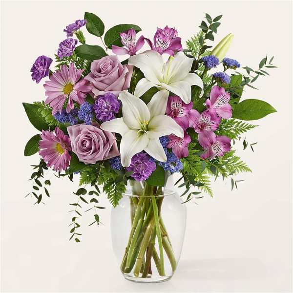 Lavender and white bouquet with lilies, roses, daisies, and alstroemeria in a clear glass vase.