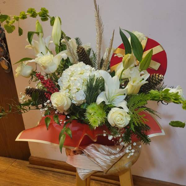 White floral arrangement with roses, lilies, and hydrangea in a red gift wrap