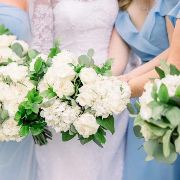 Bridesmaids holding white rose bouquets with greenery