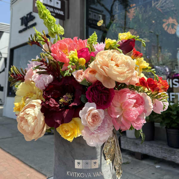Large mixed bouquet of pink, peach, yellow, and burgundy flowers in a gray hatbox