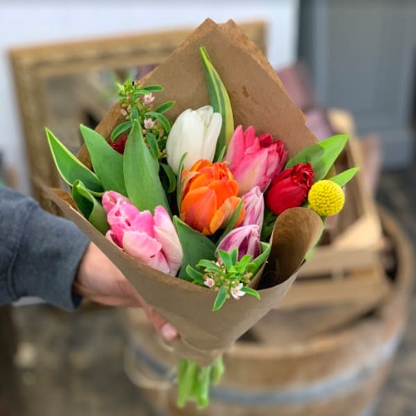 Handheld bouquet of colorful tulips wrapped in brown paper