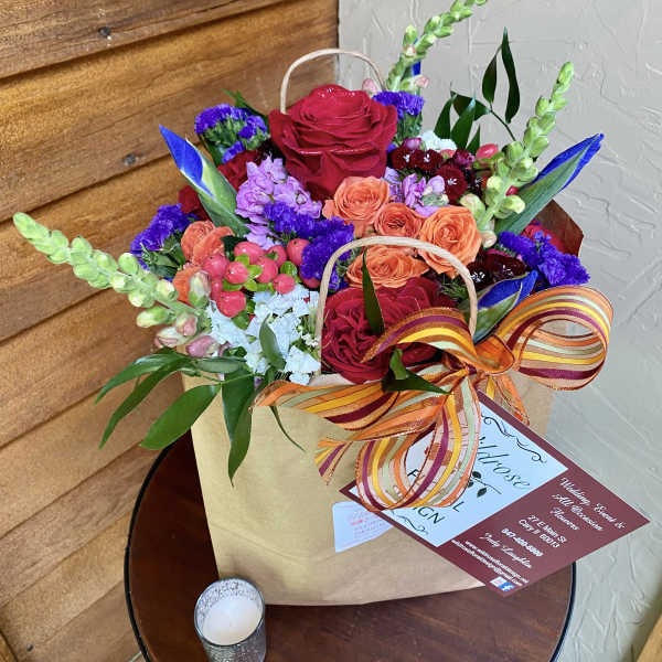 Mixed bouquet of red, orange, purple, and blue flowers in a gift bag