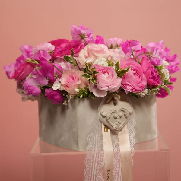 Pink floral arrangement in a gray hatbox with lace ribbon and heart ornament
