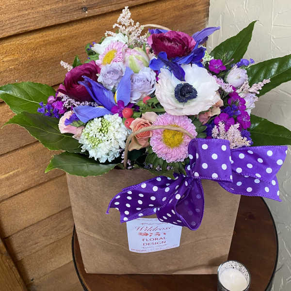 Colorful mixed flower arrangement in a kraft bag with a purple polka dot bow.