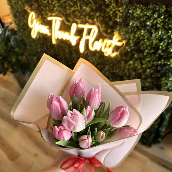 Pink tulip bouquet wrapped in pale paper with a red ribbon
