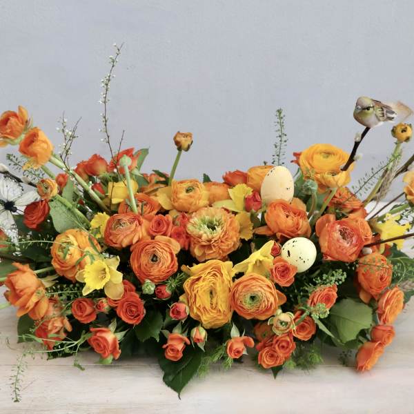 Orange and yellow floral arrangement with decorative eggs and bird accents