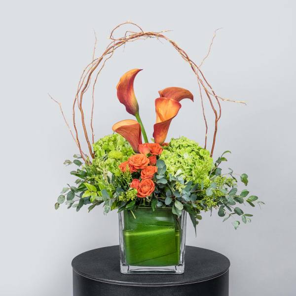 Orange calla lilies and roses in a square glass vase with green hydrangeas