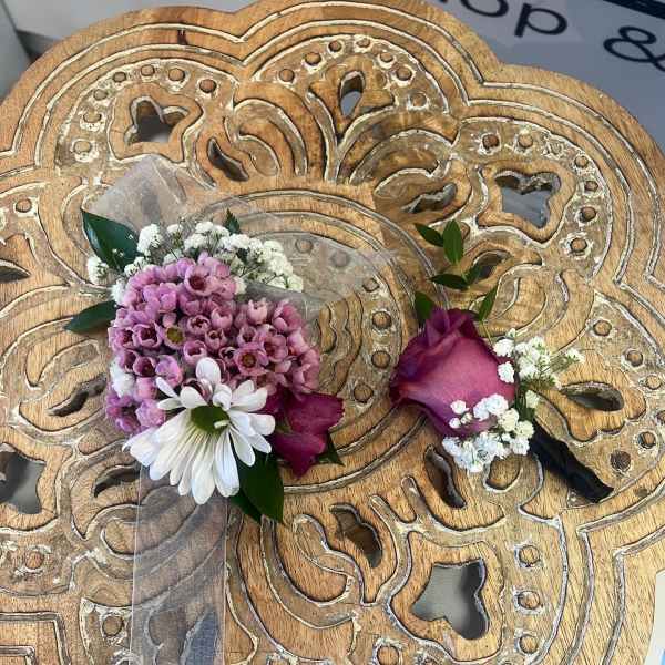Pink and white corsage and boutonniere set on a carved wooden table