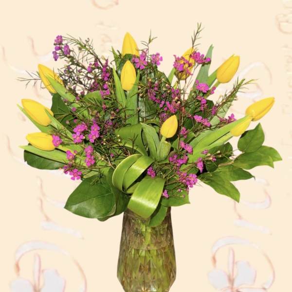 Yellow tulips and pink filler flowers in a glass vase