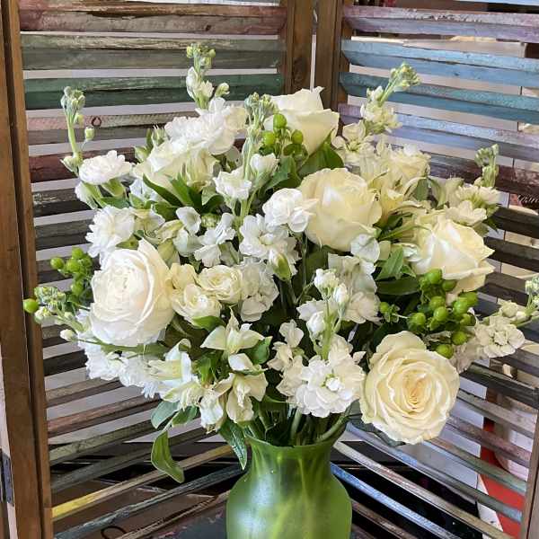 White roses and small white flowers arranged in a green vase