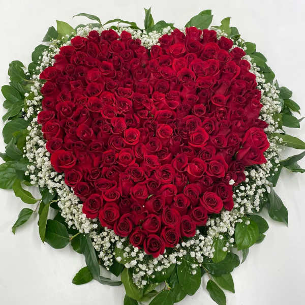 Heart-shaped arrangement of red roses framed by white filler flowers and green foliage