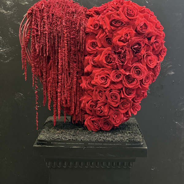 Heart-shaped red rose arrangement with cascading red strands on a black pedestal