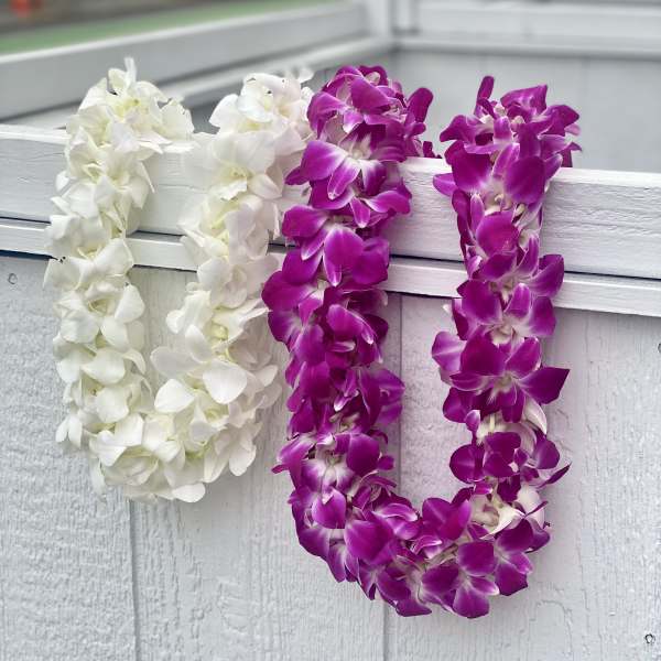 Two orchid leis draped over a white railing, one white and one purple.