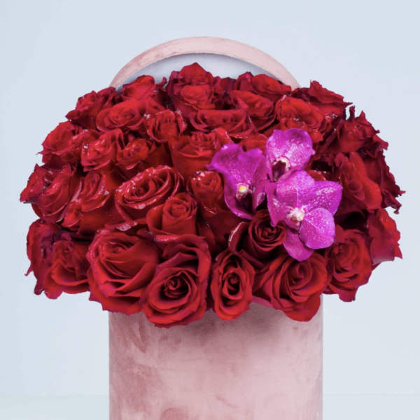 Red roses in a pink cylindrical box with purple orchids