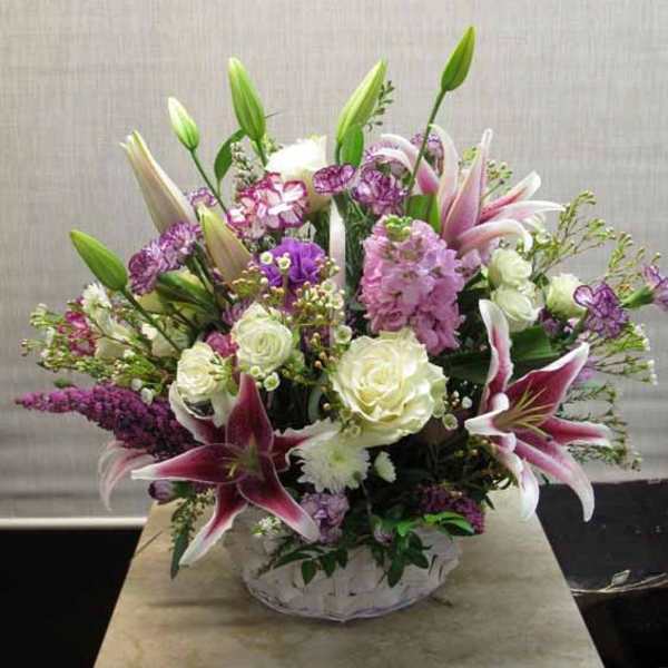 Mixed bouquet of lilies, roses, and purple flowers in a white vase