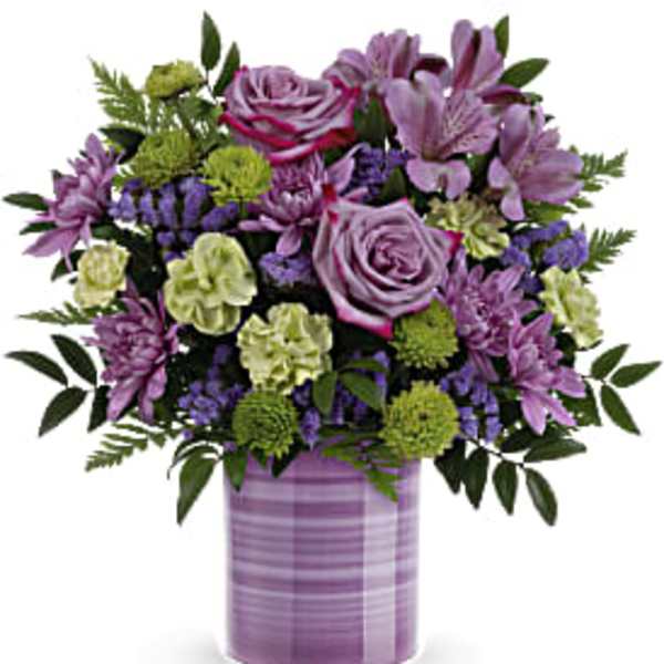 Mixed bouquet of purple roses and blooms with green accents in a lavender striped cylinder vase