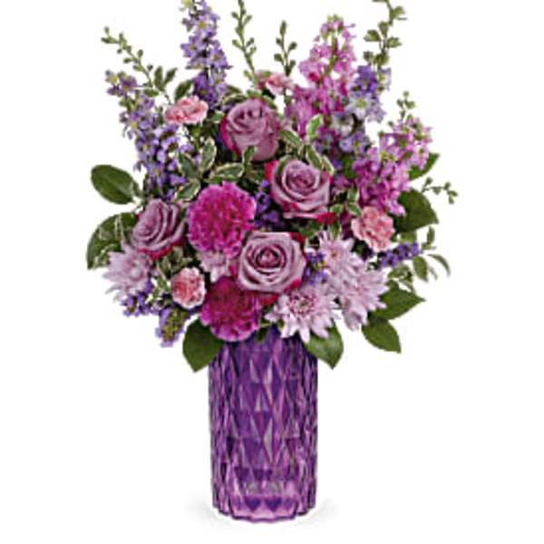 Purple and pink mixed flower arrangement with roses and carnations in a tall purple glass vase