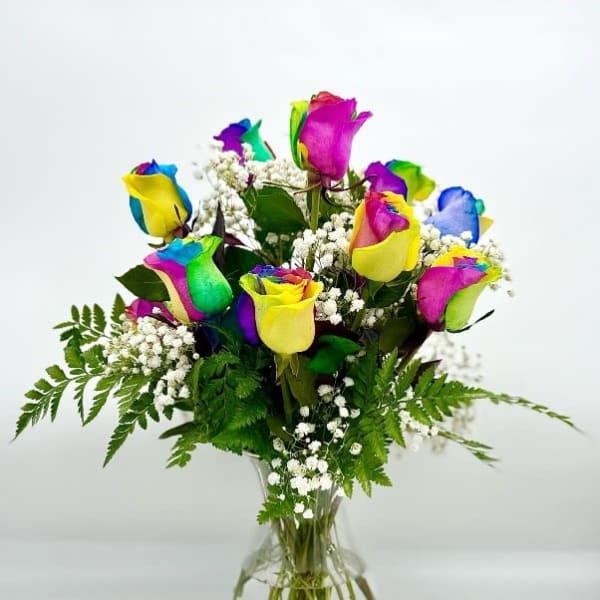 Rainbow-colored roses in a clear glass vase with baby's breath