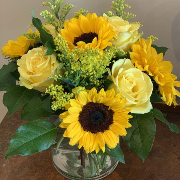 Yellow sunflowers and roses arranged in a clear glass vase