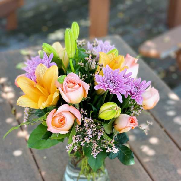 Bouquet of pink roses, yellow lilies, and purple chrysanthemums in a glass vase